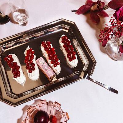 Un ruj Lancome așezat printre patru deserturi cu cremă decorate cu coacăze roșii pe o tavă de argint.