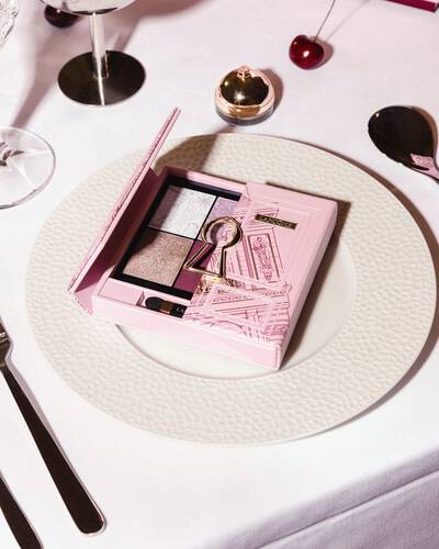 O paletă roz de farduri de pleoape Lancome cu un design auriu cu găuri de cheie, prezentată elegant pe o farfurie albă de cină.