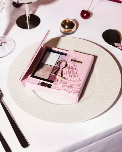 O paletă roz de farduri de pleoape Lancome cu un design auriu cu găuri de cheie, prezentată elegant pe o farfurie albă de cină.