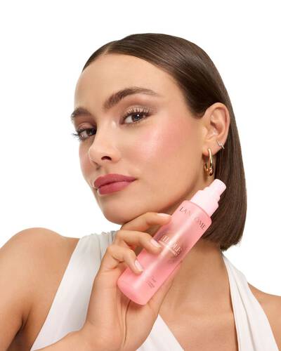Femeie cu un bob elegant ținand spray-ul de fixare a machiajului Lancome Idole.