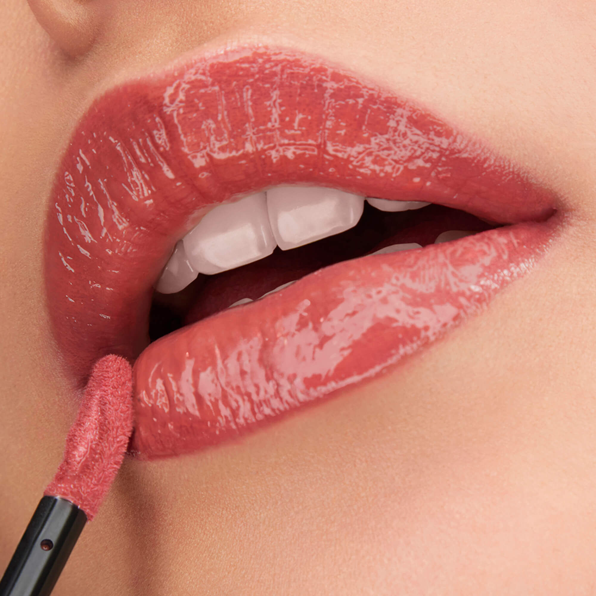 Un prim-plan cu buze lucioase, roz nude, evidențiate cu aplicatorul produsului Lancome L'Absolu Rouge Glaze Tintation pentru un aspect lucios, ca de glazură.