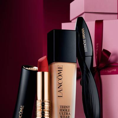 Natură statică elegantă formată din rujul mat L'Absolu Rouge de la Lancome, fondul de ten Teint Idole Ultra Wear și mascara Hypnose Drama, pe un fundal premium roșu inchis de sărbători.