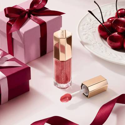 Luciu de buze Lancome in tonuri de fructe de pădure, intr-un tub hexagonal premium, decorat cu cutii cadou și cireșe.