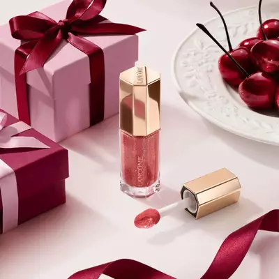 Luciu de buze Lancome in tonuri de fructe de pădure, intr-un tub hexagonal premium, decorat cu cutii cadou și cireșe.