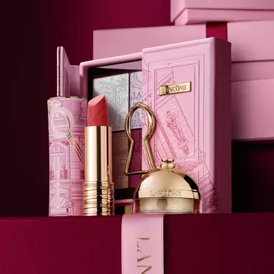 Un set cadou de sărbători Lancome selectat, care include ruj, paletă de farduri de pleoape și produse de infrumusețare aurii expuse pe o carcasă decorativă roz.