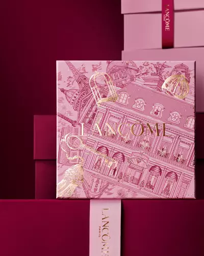 Imagine cu cutia de cadouri roz Lancome stand in fața unui teanc de cutii roz și roșu inchis, așezate pe un fundal roșu inchis.