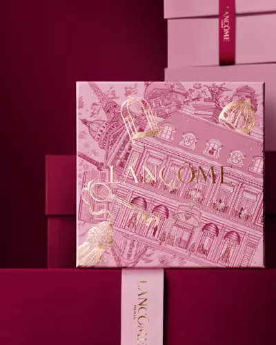 Imagine cu cutia de cadouri roz Lancome stand in fața unui teanc de cutii roz și roșu inchis, așezate pe un fundal roșu inchis.