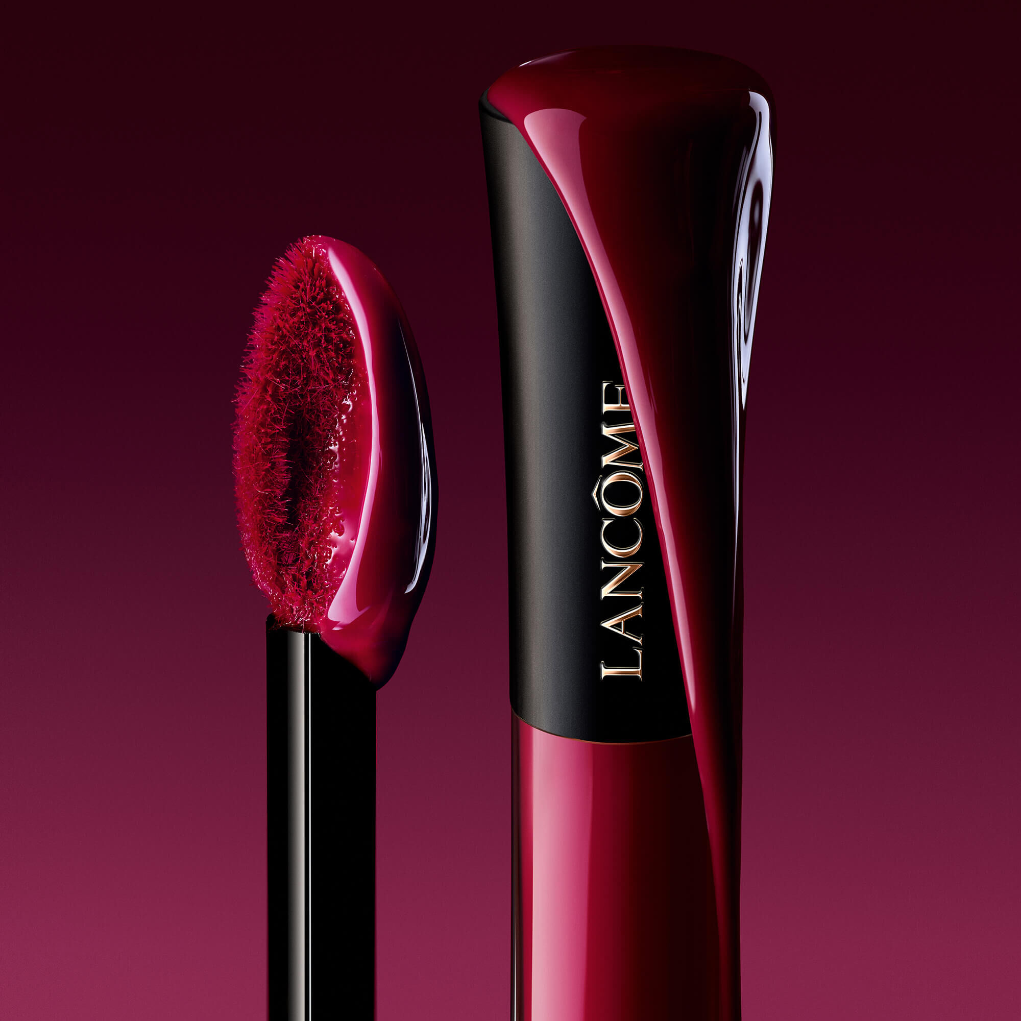 Un prim-plan artistic al unui recipient Lancome L'Absolu Rouge Glaze Tintation cu un pigment bogat și lucios care curge pe lateral, langă un aplicator saturat cu produs.