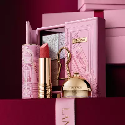 Un set cadou de sărbători Lancome selectat, care include ruj, paletă de farduri de pleoape și produse de infrumusețare aurii expuse pe o carcasă decorativă roz.