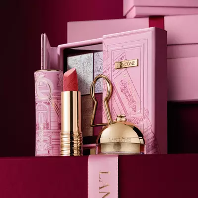 Un set cadou de sărbători Lancome selectat, care include ruj, paletă de farduri de pleoape și produse de infrumusețare aurii expuse pe o carcasă decorativă roz.