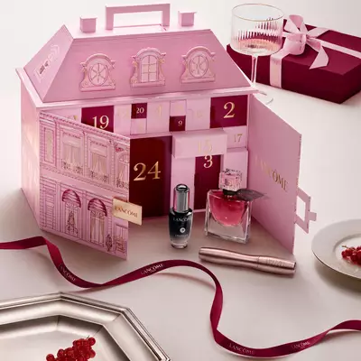 Un calendar advent Lancome in formă de clădire elegantă pariziană deschis, expus alături de produse de infrumusețare și o fundă roșie.