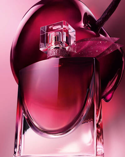 Close-up artistic: sticla vișinie de parfum, poziționată in fața unei cireșe mari și lucioase.
