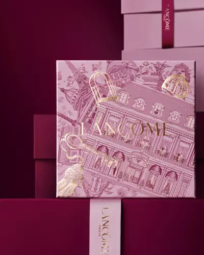 Imagine cu o cutie de cadou de sărbători Lancome, de culoare roz, amplasată in fața unui teanc de cutii de cadou roz și roșu inchis, pe un fundal roșu inchis.