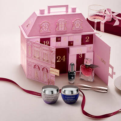 Un calendar advent Lancome in formă de clădire elegantă pariziană deschis, expus alături de produse de infrumusețare și o fundă roșie.