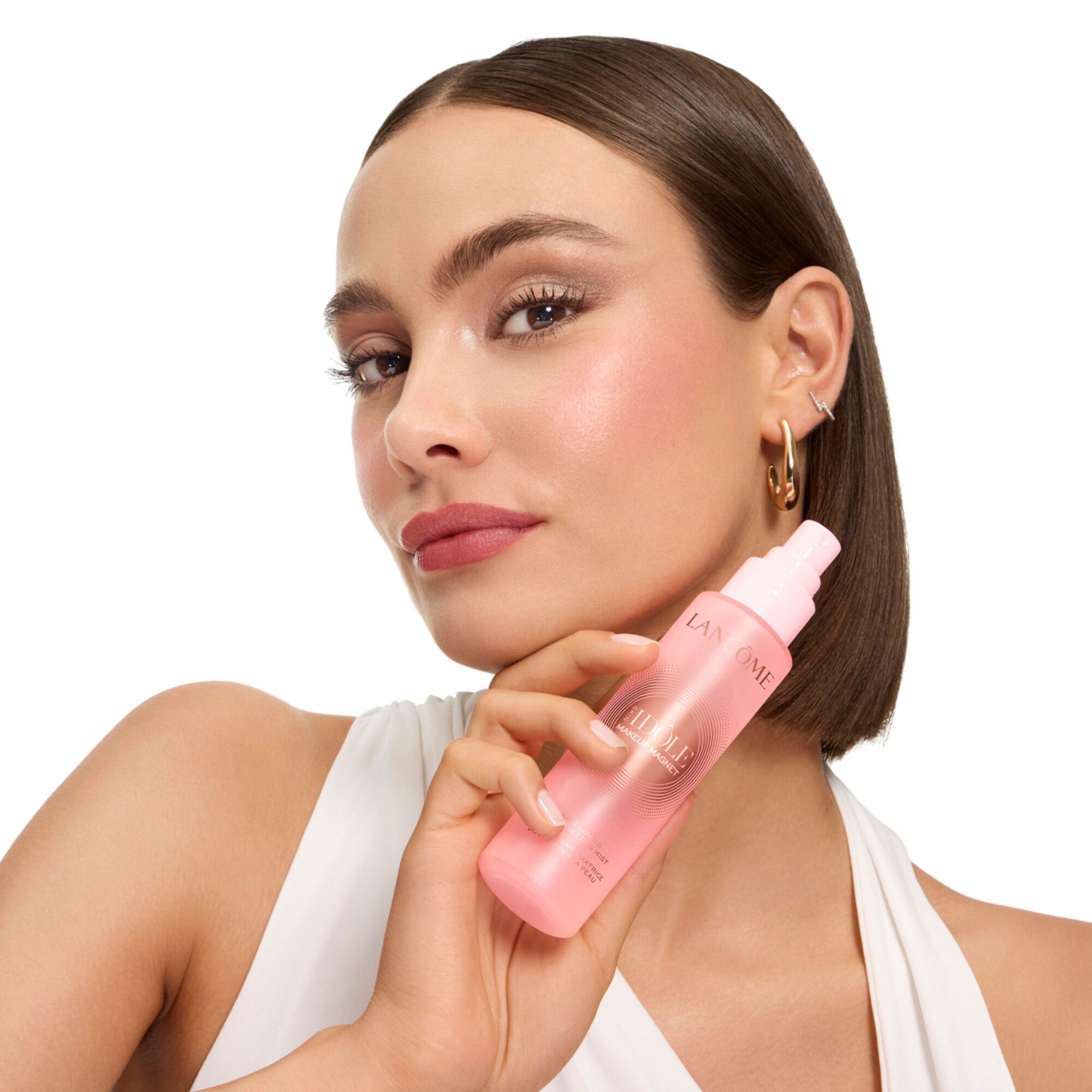 Model ținand spray-ul de fixare Idole langă față.