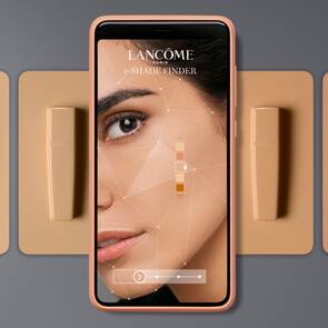 O imagine care prezintă un telefon mobil ce afișează aplicația e-Shade Finder de la Lancome, alături de un cod QR și mai multe nuanțe de fond de ten.