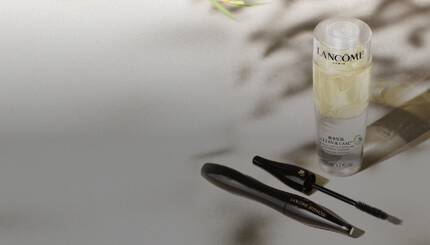 Produse cosmetice Lancome: un flacon de demachiant și un rimel, așezate pe o suprafață elegantă.