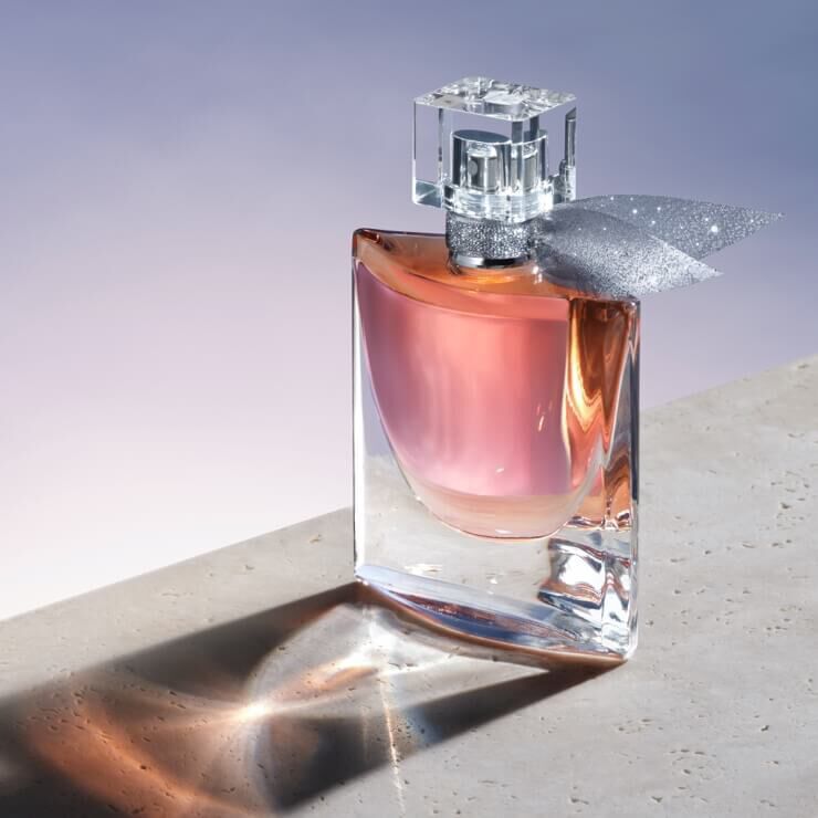 Flacon de parfum elegant, cu un capac decorat și un fundiță din satin, așezat pe o suprafață neutrală, reflectand lumina.