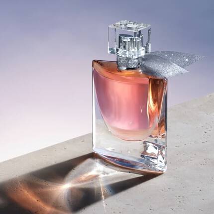 Flacon de parfum elegant, cu un capac decorat și un fundiță din satin, așezat pe o suprafață neutrală, reflectand lumina.