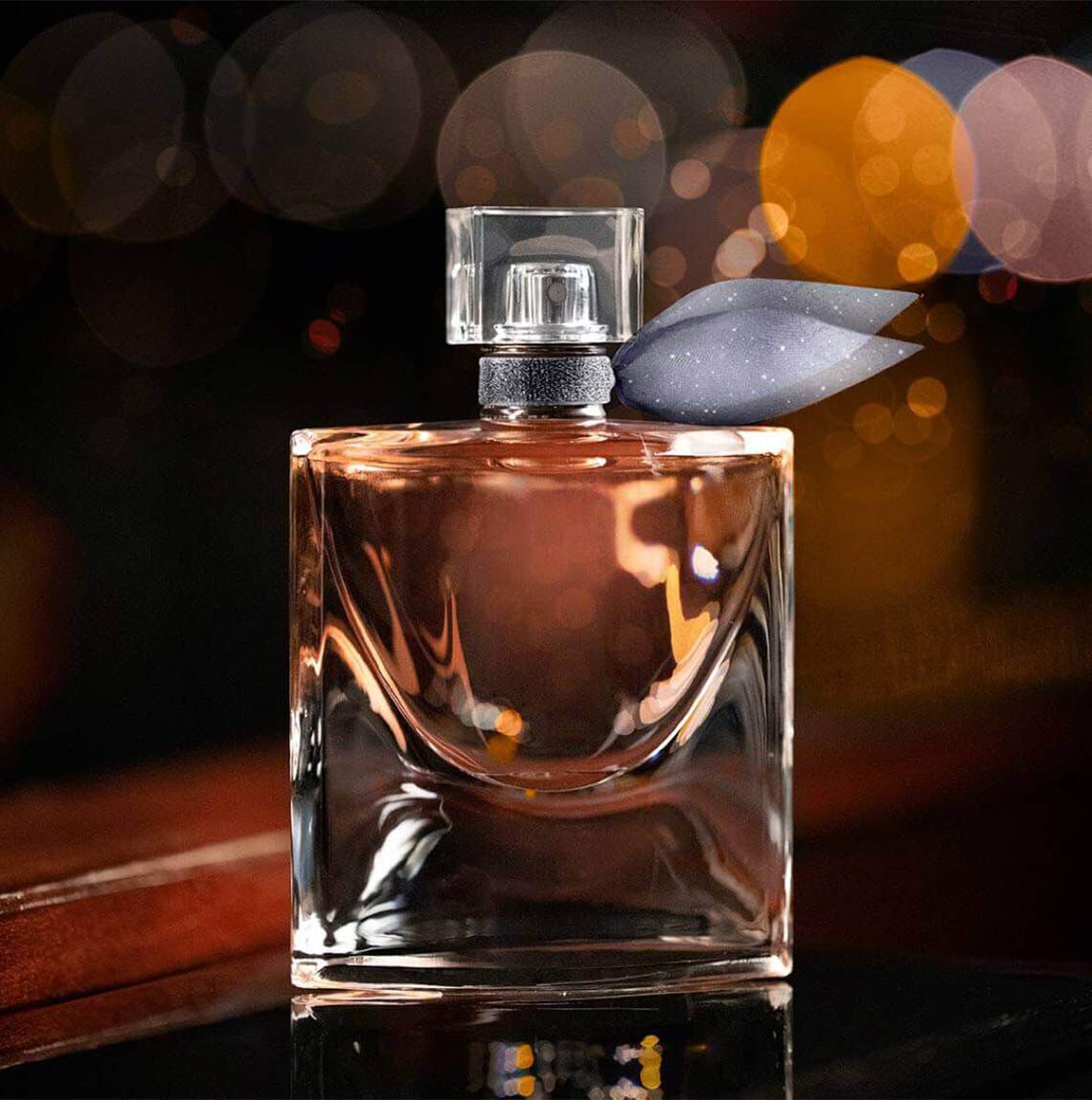 Flacon de parfum elegant, cu o formă rectangulară, așezat pe o suprafață lucioasă, iluminat de lumini calde de fundal.