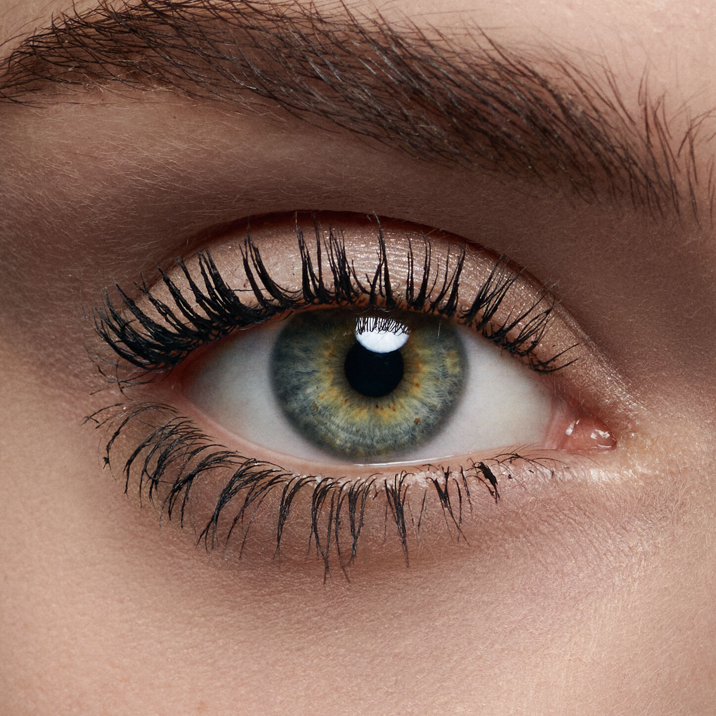 Close-up of a human eye, showcasing a mix of green and brown iris colors, long eyelashes, and a clear, shiny cornea.