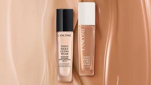 Două flaconuri de fond de ten Lancome Teint Idole Ultra Wear, unul cu capac negru și altul cu capac alb, pe un fundal de nuanță nude.