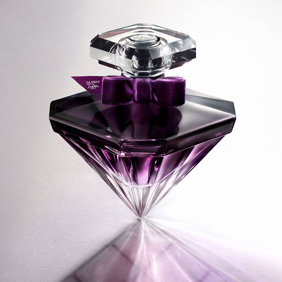 Sticla de parfum cu un design elegant in formă de diamant, cu un capac transparent și un fundal luminos.