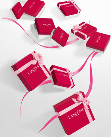 Alt text: A collection of red Lancome gift boxes with white lids, some adorned with pink ribbons and flowers, arranged playfully on a white background.
