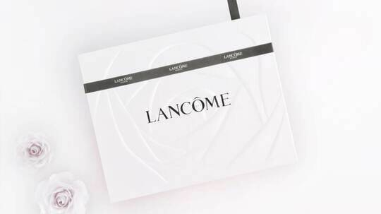 Cutie albă elegantă Lancome, decorată cu un fundal de trandafir și panglică neagră, pe fond alb.