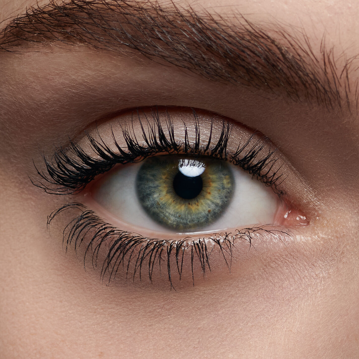 Close-up of a human eye with vivid green and brown hues, long eyelashes, and a subtle sheen.