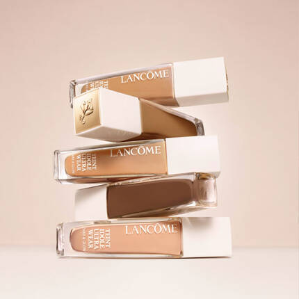Patru flacoane de fond de ten Lancome, aranjate unul peste altul, pe un fundal neutru.