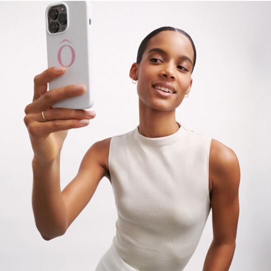 Femeie zambind in timp ce iși face un selfie cu un telefon mobil, purtand un top fără maneci.