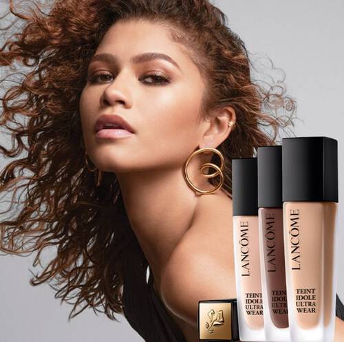 Femeie cu părul buclat și cercei mari, promovand fondul de ten Lancome Teint Idole Ultra Wear.
