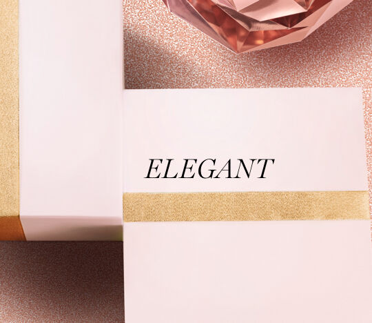 Two elegant gift boxes with a gold accent, placed on a textured pink background, alongside a faceted rose-colored crystal.