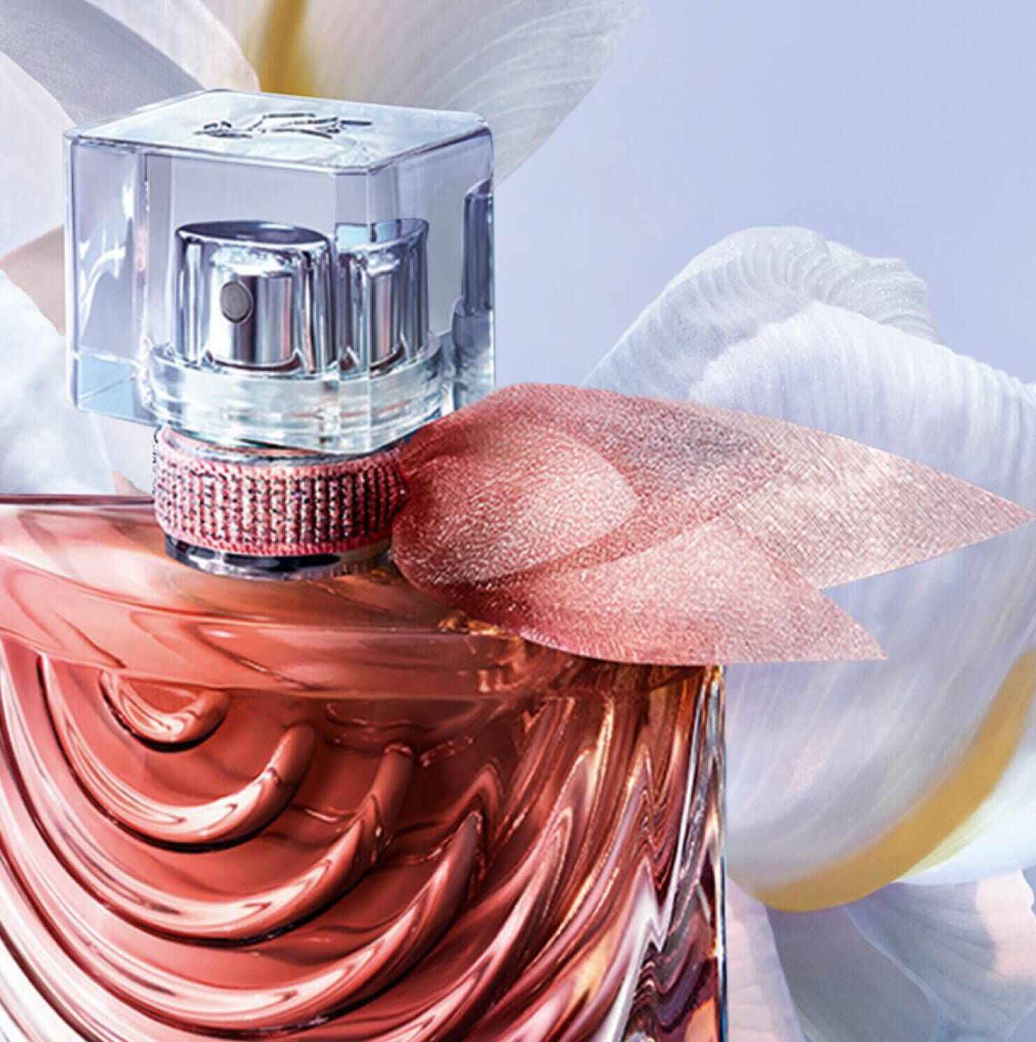 A close-up of a stylish perfume bottle with a textured coral-colored liquid, featuring a clear cap and a pink ribbon accent, set against a soft floral background.
