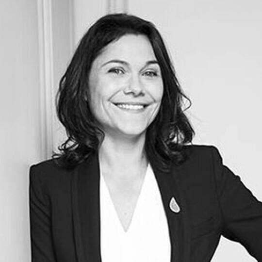 A smiling woman with shoulder-length dark hair wearing a blazer, posing confidently against a plain background.