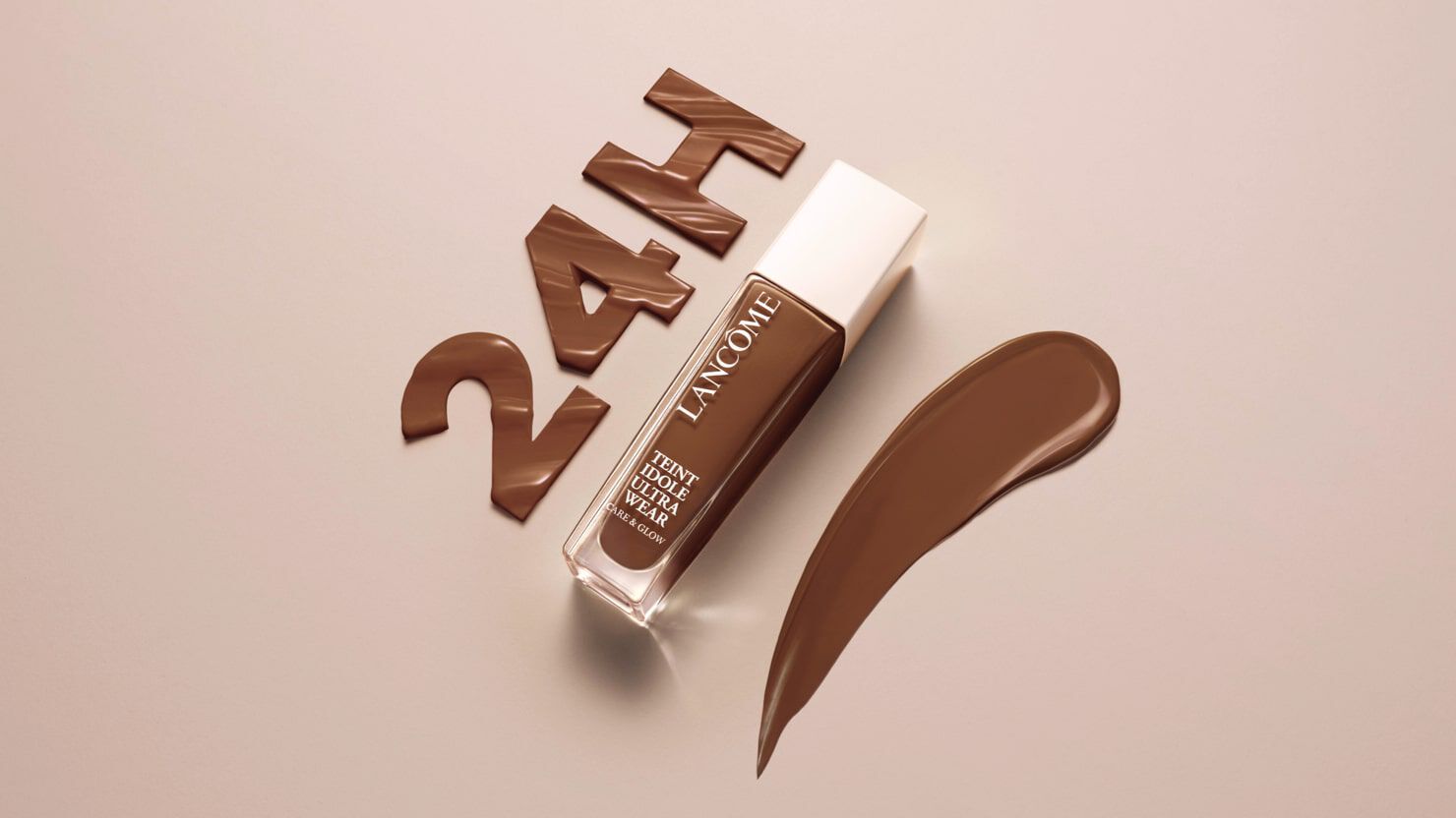 A bottle of Lancome foundation in a deep brown shade, with a swatch of the product beside it and the text "24H" made from chocolate-colored material in the background.