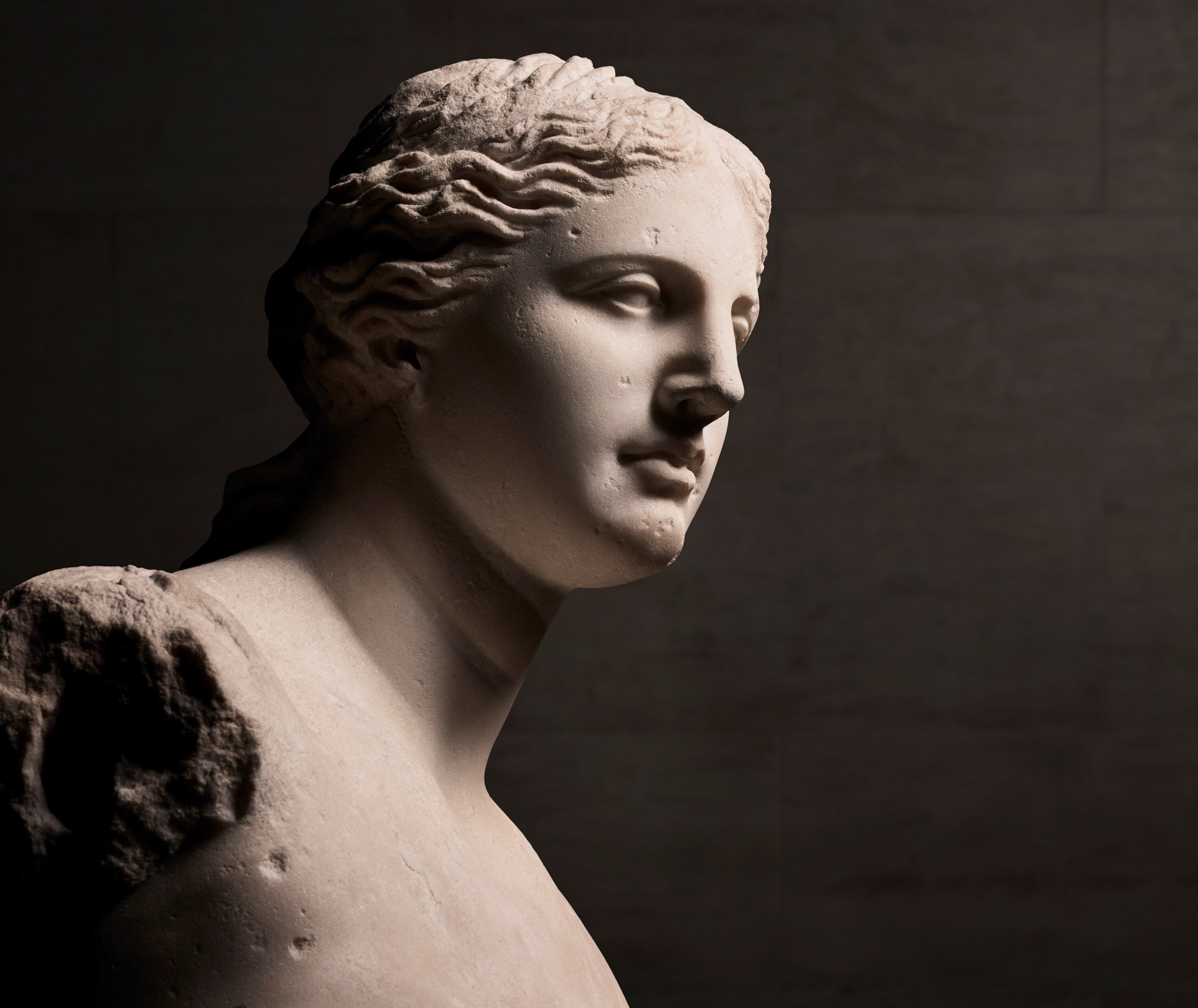 Statuie de marmură a unei femei, iluminată dintr-o parte, evidențiind detalii ale feței și părului.