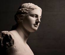 Statuie de marmură a unei femei, iluminată dintr-o parte, evidențiind detalii ale feței și părului.