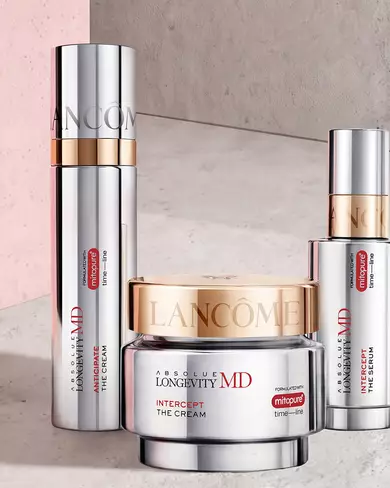 Imaginea prezintă un dispozitiv de testare a nuanței fondului de ten Lancome, plasat in fața mai multor flacoane de fond de ten Lancome, fiecare cu nuanțe diferite.