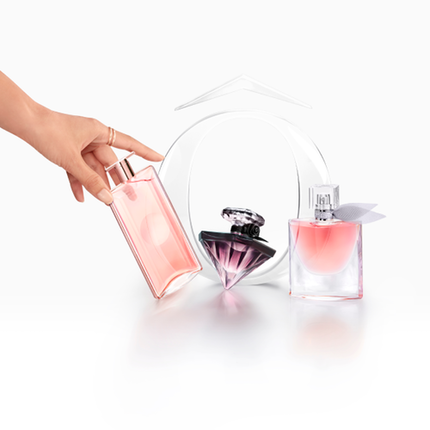 O mană care ține un parfum roz, alături de două alte sticle de parfum, pe un fundal alb.