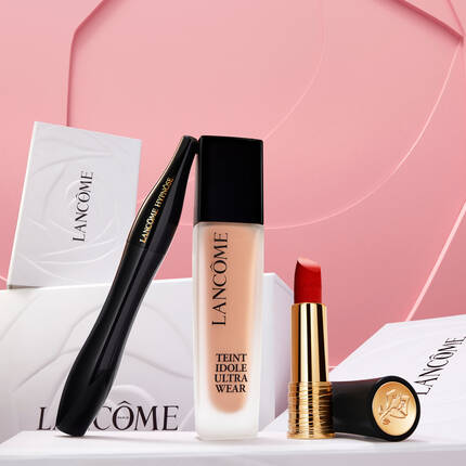 Text alternativ: O mană care incadrează produse de machiaj Lancome, inclusiv un fond de ten, o ruj și o cutie cu logo-ul brandului, pe un fundal roz.