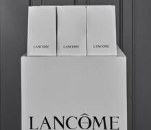 Cutii albe de produse Lancome, așezate pe un suport cu logo-ul Lancome.