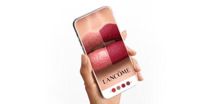 O persoană ținand un telefon mobil care afișează diferite nuanțe de ruj de la Lancome pe buze.