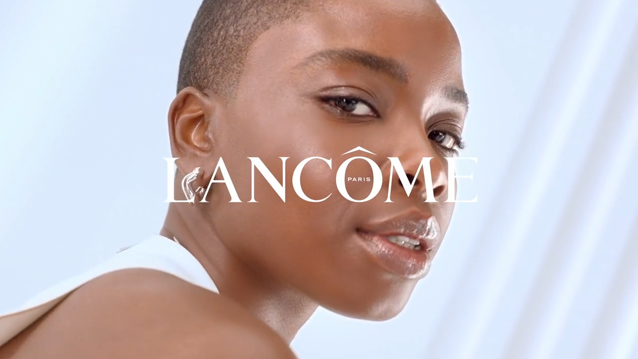 Reclamă Lancome Paris cu un model cu părul scurt, privind către cameră, având un ten strălucitor.