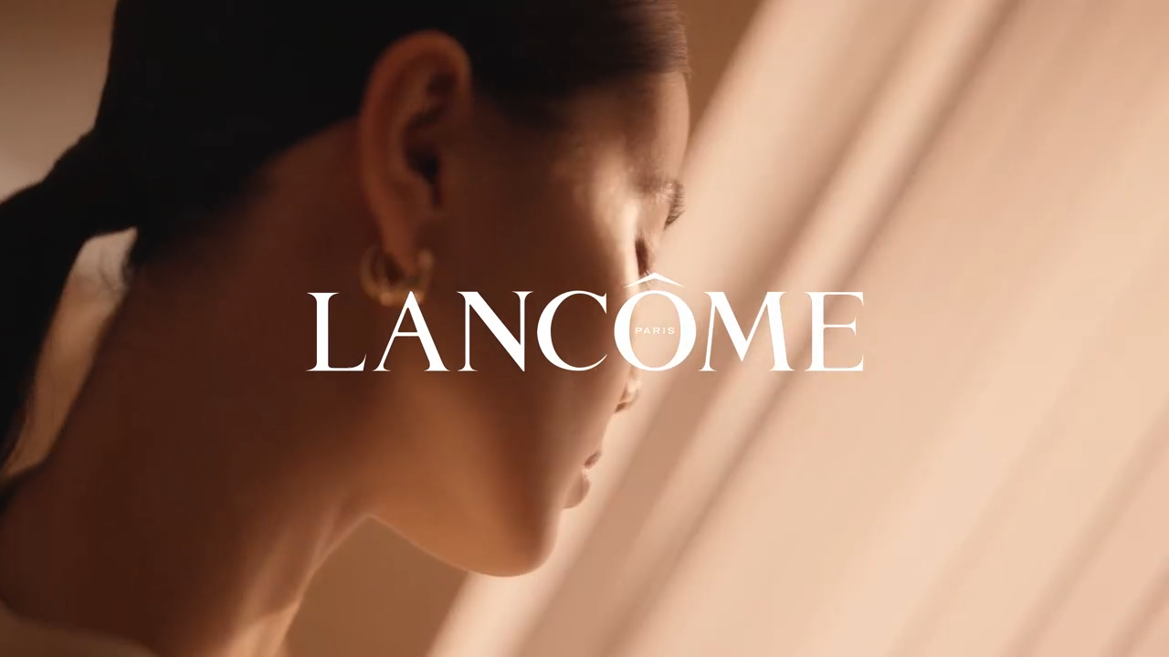 Femeie tânără cu părul prins, contemplând, în fundal clar și logo-ul Lancôme.
